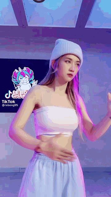 a woman wearing a white crop top and a white beanie is standing in front of a sign that says tik tok .