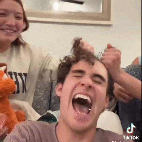 a group of people are playing with a man 's hair while a woman holds a stuffed animal .