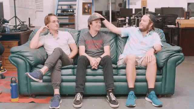 three men are sitting on a green couch and one of them has a shirt that says never give up on it