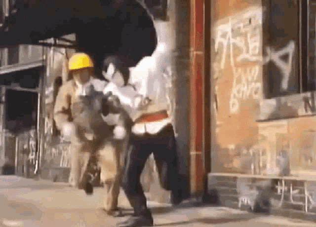 a man wearing a hard hat is fighting another man on the street