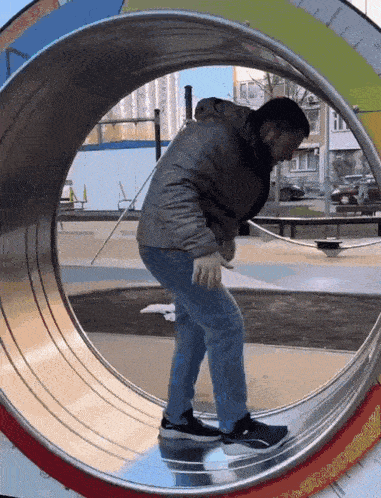 a man in a gray jacket is walking through a metal tube in a park