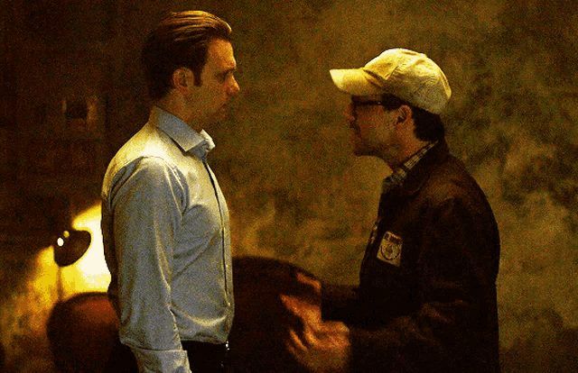 two men are standing next to each other and one has a patch on his jacket that says ' us postal service ' on it