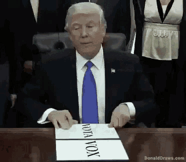 donald trump is sitting at a table with a sign that says vota vox
