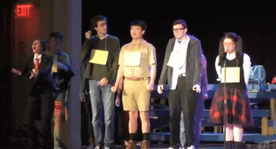 a group of people standing on a stage with an exit sign in the background