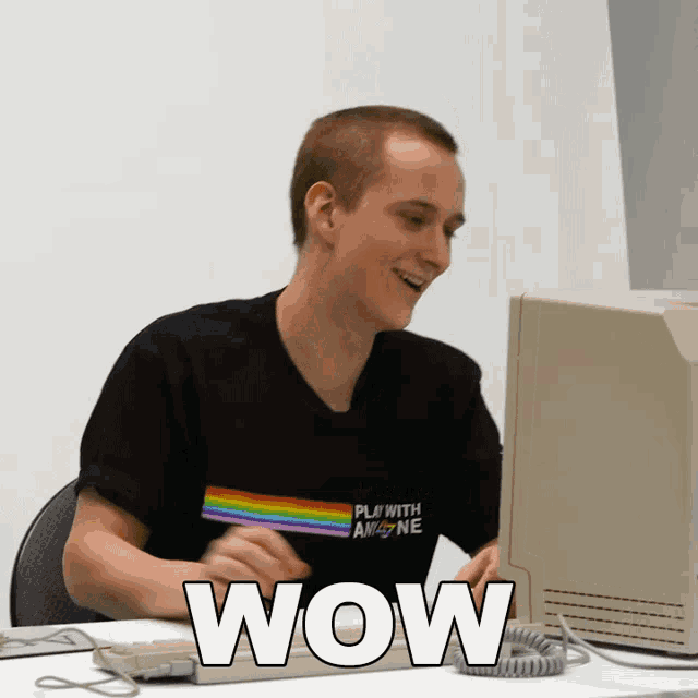 a man wearing a black shirt that says " play with anyone " is typing on a keyboard