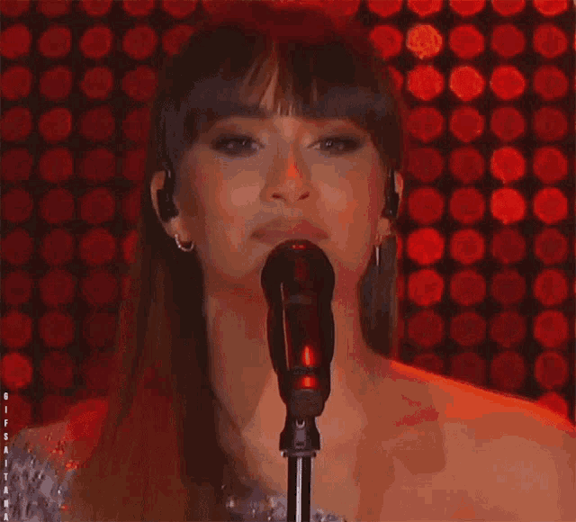 a woman singing into a microphone in front of a red background