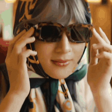 a woman wearing sunglasses and a scarf around her head is talking on a cell phone
