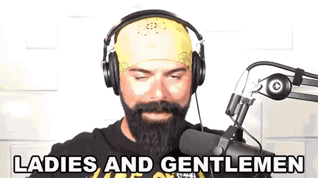 a man wearing headphones and a bandana stands in front of a microphone and says ladies and gentlemen