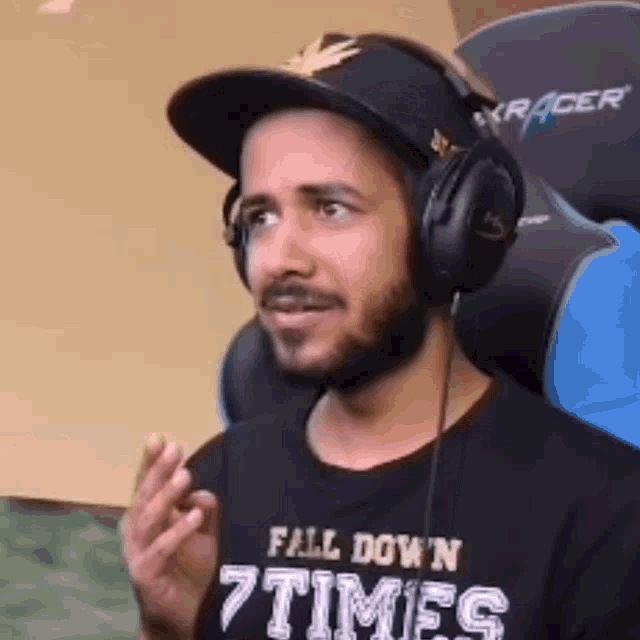 a man wearing headphones and a hat is wearing a shirt that says `` fall down 7 times '' .