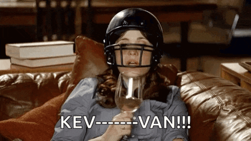 a woman wearing a football helmet is sitting on a couch holding a glass of wine and saying " kev van "