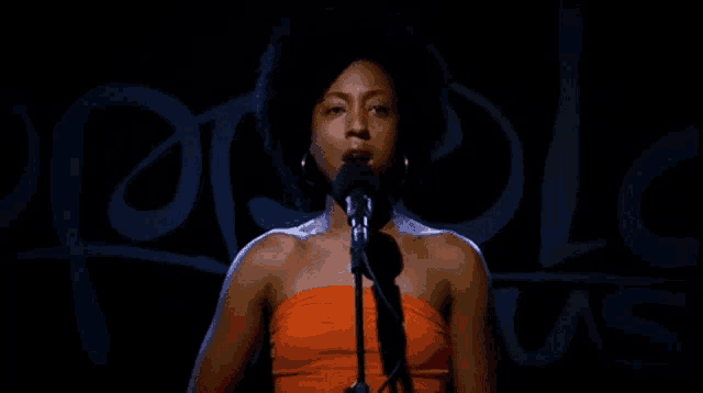a woman singing into a microphone in front of a sign that says " people "