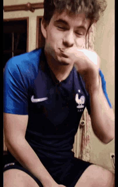 a young man wearing a blue nike shirt is making a face