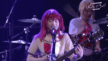 a girl with red hair is singing into a microphone while another girl plays the drums