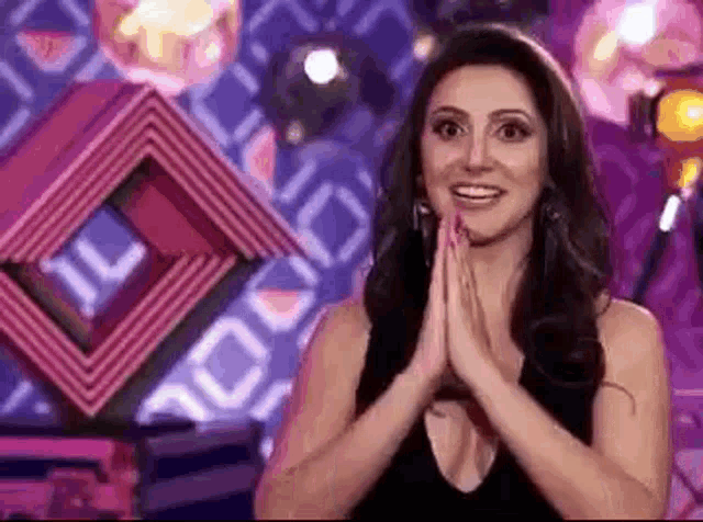 a woman is smiling with her hands folded in front of a pink and purple background .