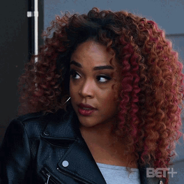 a woman with curly red hair is wearing a black leather jacket and says okay