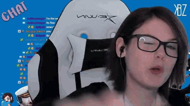 a woman wearing glasses stands in front of a white chair with the word chat on the bottom right