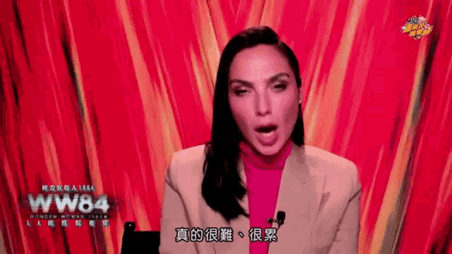 a woman in a suit and pink turtleneck is speaking into a microphone .