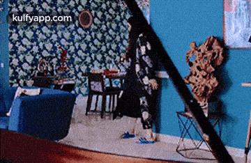 a woman is walking through a living room with a blue couch and a table .