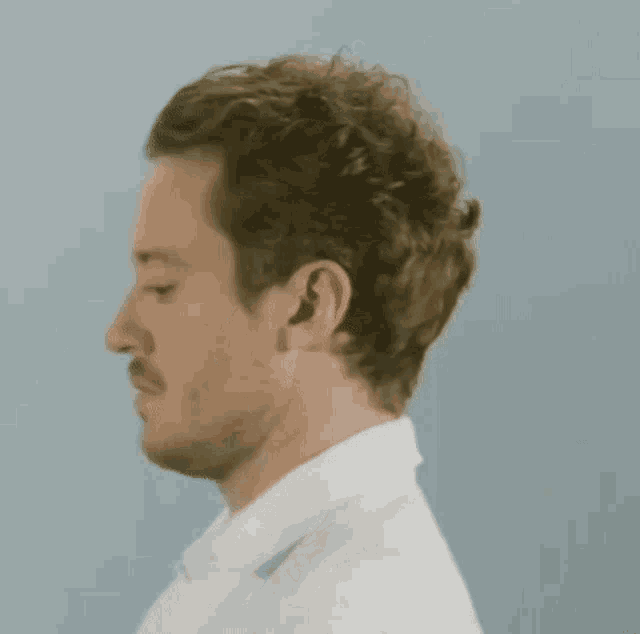 a man with curly hair and a beard is wearing a white shirt .