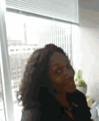 a woman with curly hair is smiling in front of a window with blinds