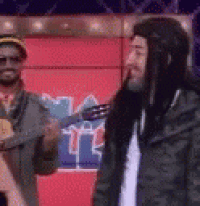 a man with long hair is playing a guitar while another man stands next to him .