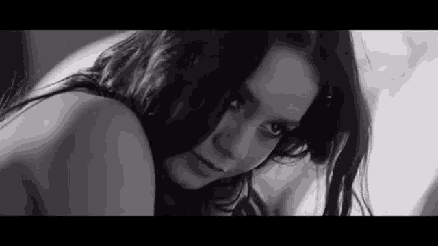 a black and white photo of a naked woman laying on a bed looking at the camera .
