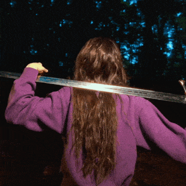 a woman in a purple sweater is holding a sword over her shoulder