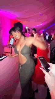 a woman in a very revealing dress is dancing in a club while a man holds a cell phone .
