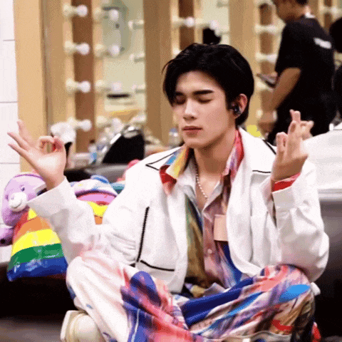 a man in a white jacket is sitting on the floor making a peace sign with his hands .