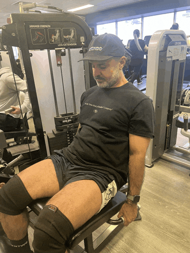 a man wearing a black t-shirt that says fends sits on a machine