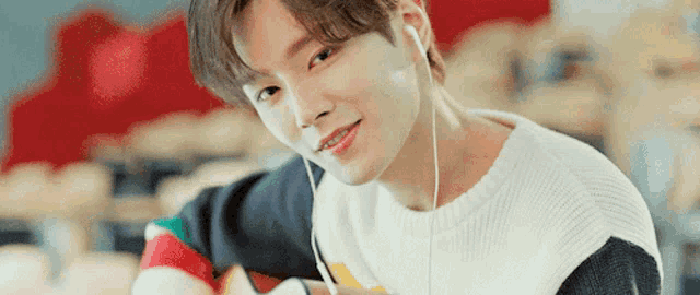 a young man wearing headphones and a sweater is looking at the camera and smiling .
