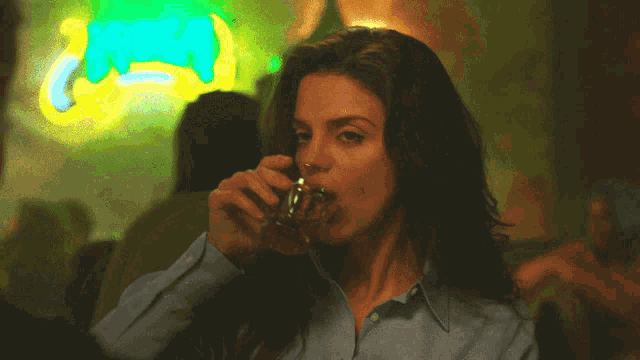 a woman drinks from a glass in front of a neon sign that says coca-cola