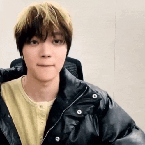 a young man wearing a black jacket and a yellow shirt is making a funny face .