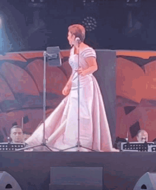 a woman in a white dress is singing into a microphone on a stage