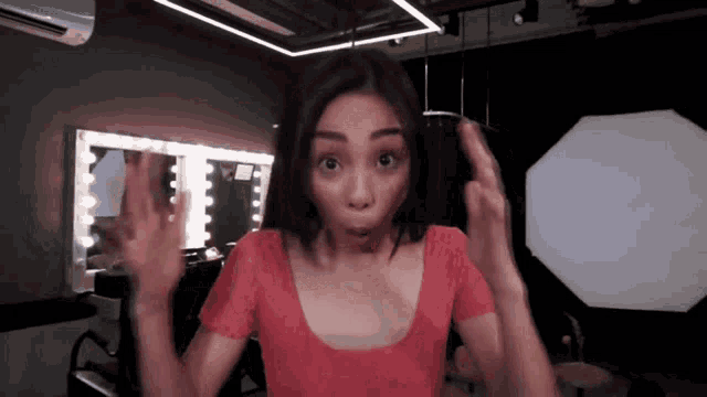 a woman in a red top is making a surprised face in front of a mirror