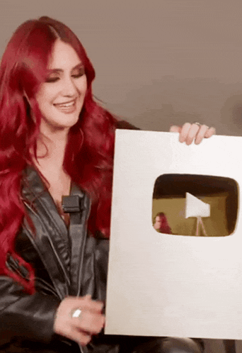 a woman with red hair is holding a sign that looks like a video camera