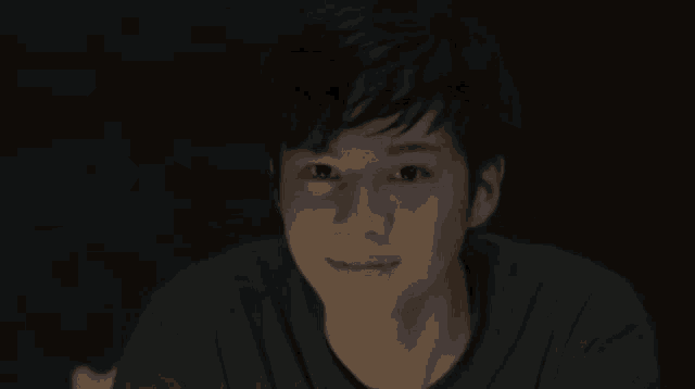 a young man in a dark room is smiling and looking at the camera