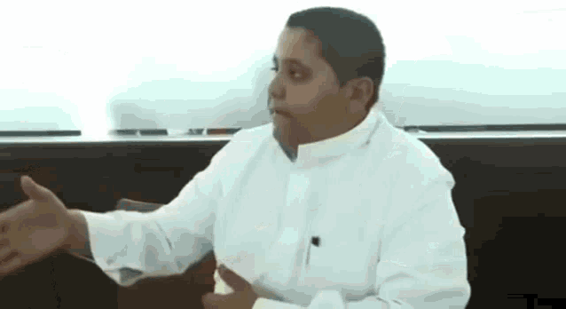 a man in a white shirt is sitting in a chair and talking to someone .