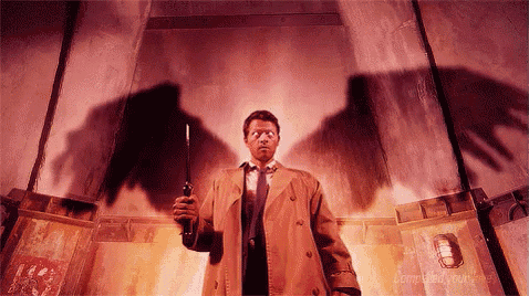 a man in a trench coat and tie is holding a gun in front of a wall with a shadow of a bird on it