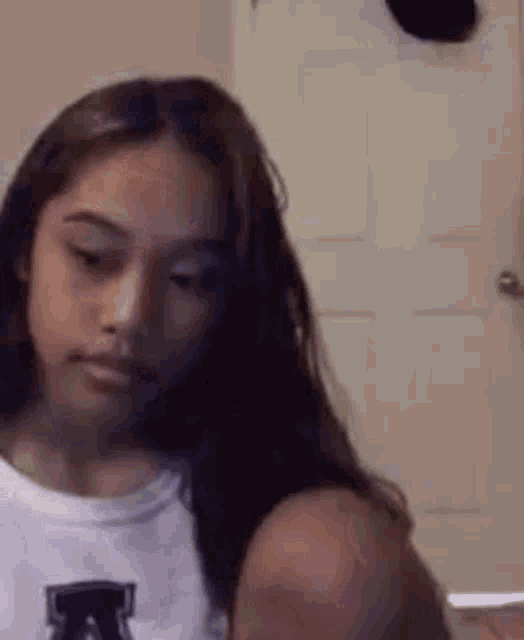 a young girl with long hair is sitting in front of a door and looking at her phone .