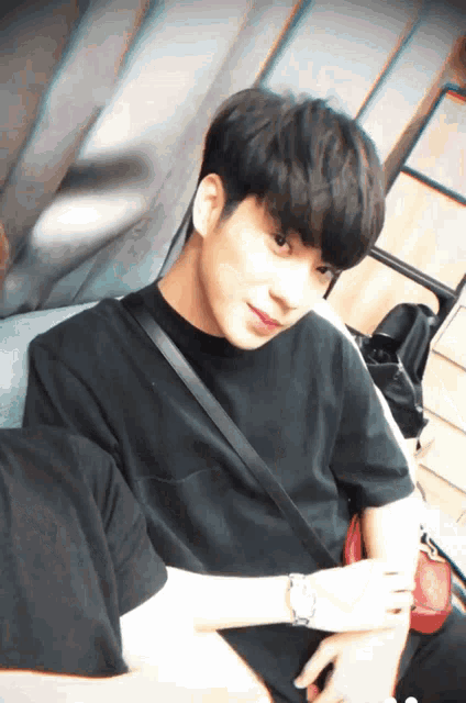 a young man wearing a black t-shirt is sitting on a couch