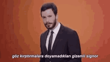 a man in a suit and tie is standing in front of an orange background and talking in a foreign language .