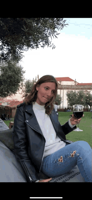 a woman in a leather jacket holds a glass of wine in her hand