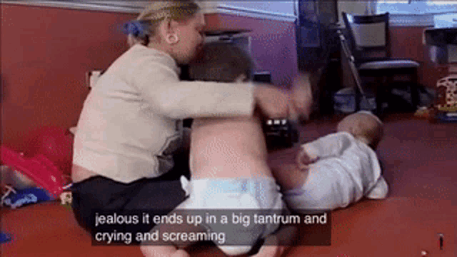 a woman is sitting on the floor with two babies and says jealous it ends up in a big tantrum and crying