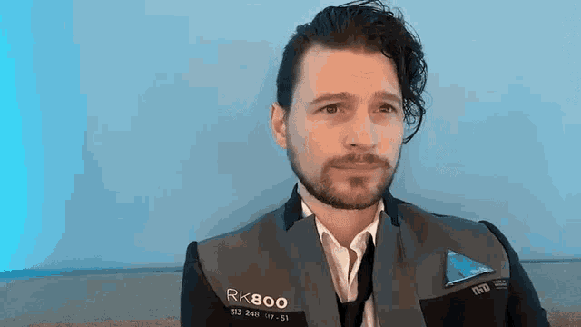 a man with a beard is wearing a suit and tie and has the letters rk800 on his jacket .