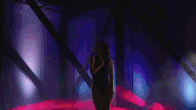a woman in a swimsuit is dancing in a dark room with purple lights .