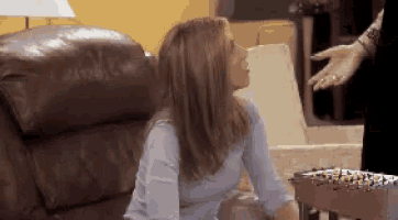 a woman is sitting on a couch talking to another woman while a man stands behind her .