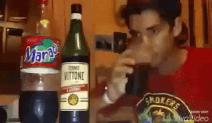 a man is drinking from a glass next to a bottle of vitone and a bottle of mango .
