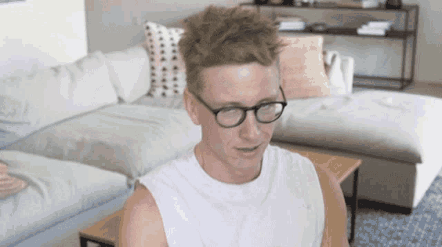 a man wearing glasses sits on a couch in a living room
