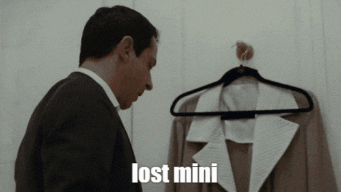 a man in a suit is looking at a jacket hanging on a hanger and the word lost mini is on the screen